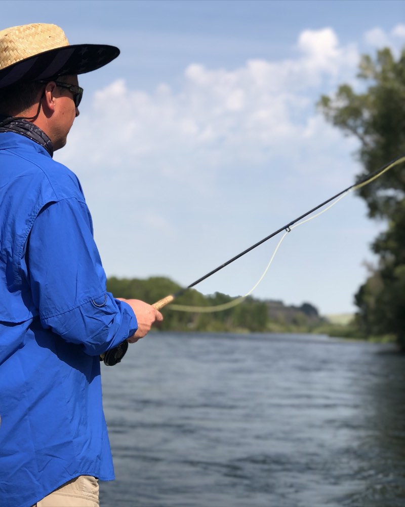 An angler casting a fly rod from a drift boat on a wide river
